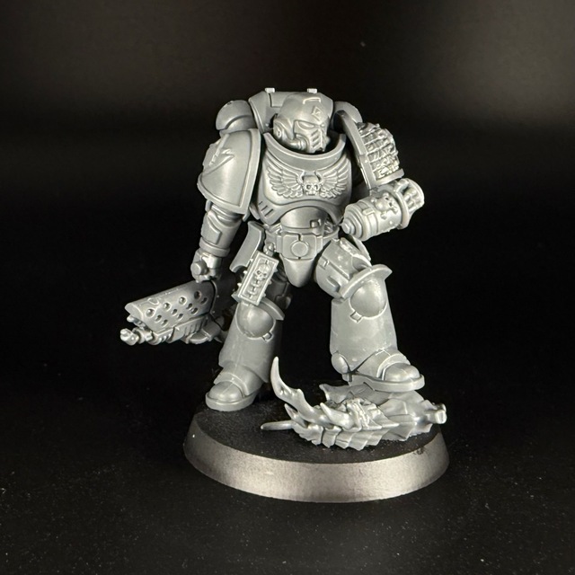 Photo of a grey plastic space marine miniature on a black background. The models right shoulder pad has a Space Wolves logo embossed on it, while the left is a covered in the embossed lettering of the Deathwatch