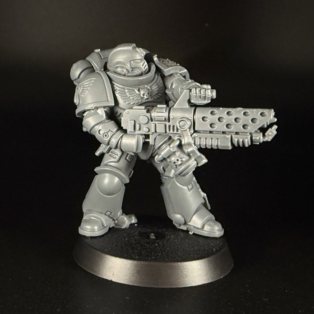 Photo of a grey plastic space marine miniature. The right shoulder pad has a raised or embossed Blood Angels icon