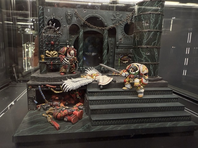 Photograph of a small scale diorama showing Horus and the Emperor, based on a classic painting from the Warhammer 40,000 lore. The Emperor is climbing a staircase with sword drawn, while Horus stands at the top over the dead body of Sanguinius, the Blood Angels primarch.