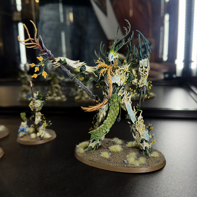 Photograph of a Sylvaneth Treelord miniature in a dark display case. The bark of the treelord is a pale bone-ish colour, with spring greens complementing in the details.