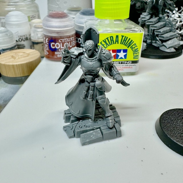 Photo of a plastic miniature with some modifications in progress. A sword has been cut away from its belt and staff cut away from the left hand. A hole is visible in the model on the right thigh where an unwanted piece has been removed.