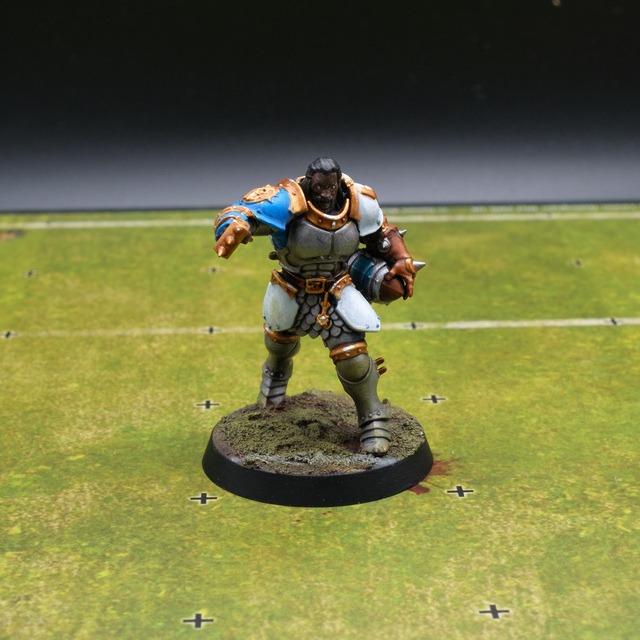 Photograph of a converted Stormcast Eternal Vindictor as a Blood Bowl blitzer, carrying a ball under one arm and punching forwards with the other. The model is standing on a section of Blood Bowl pitch.