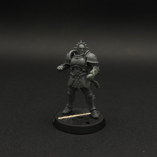 Photograph of a grey plastic, unpainted miniature. Patches of green stuff can be seen on the left forearm where gaps have been filled while converting the miniature. The slot in the base has also been filled with a portion of matchstick.