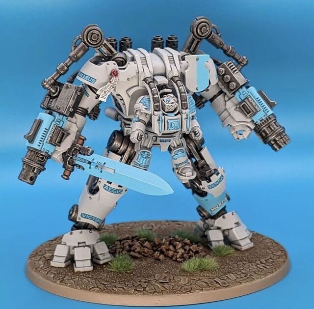 Photograph of a Grey Knight Nemesis Dreadknight model on a blue background. The model has been painted with a warm off-white/pale grey base and baby blue accents on the runes, sword blade, etc.