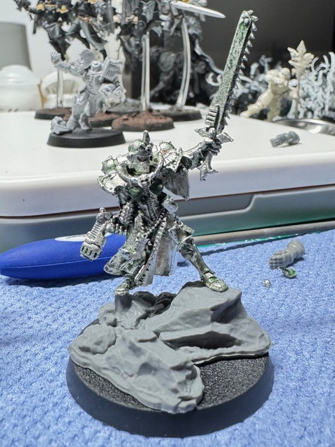 Photo of the Sisters of Battle model with new green stuff applied to reconstruct the chest, now re-based on a more scenic larger base, standing astride large rocky outcrop