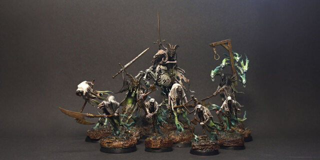 Dark, moody photograph of a selection of Nighthaunt miniatures: various ghouls painted in dirty off-white tattered fabrics that blend to glowing green wisps of energy, on muddy brown bases.