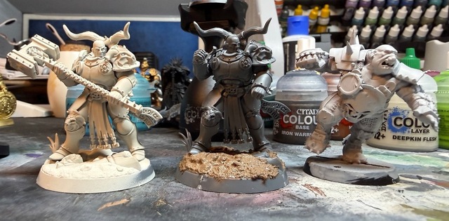 Photo of three miniatures lined up side-by-side: a white-primed Rostus Oxenhammer model, a grey unpainted Rostus model that’s had the hammer removed to look more like a Blood Bowl player, and a white-primed Blood Bowl ogre. The Rostus models are taller than the ogre.