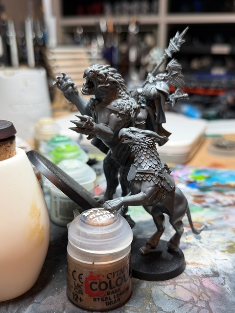 Photograph showing the evocator on dracoline angled steeply up against a painting handle to see its height, with a gryph-charger model similarly angled up alongside it. The gryph-charger only comes up to the dracoline's shoulder