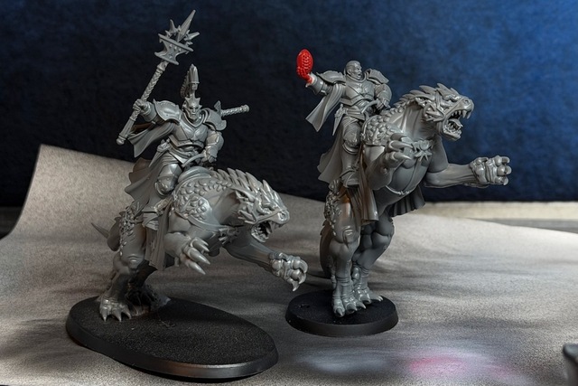 Photography of two Evocator on Dracoline models (the sculpt with the dracoline leaping forward, front claws reaching out). The copy on the right is on a much smaller 40mm round base, though, with the dracoline angled almost standing straight up so it looks more like it’s roaring a challenge than leaping at a victim. The rider holds a ball upright in one hand, rather than the staff on the original and the converted rider has an un-helmeted head looking in the same direction as the dracoline instead of off to the side