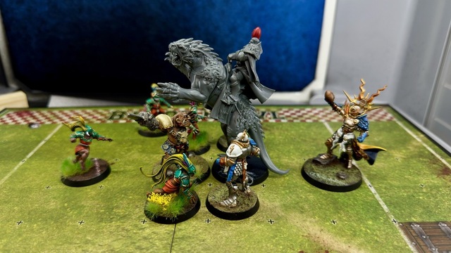 Photo of a Blood Bowl pitch with players lined up against each other: Amazons on the left and Stormcast Eternals on the right, with the metal Morg ‘n‘ Thorg mini up against the dracoline. Everything fits in a grid square, though the dracoline’s tail sticks out into the square behind it