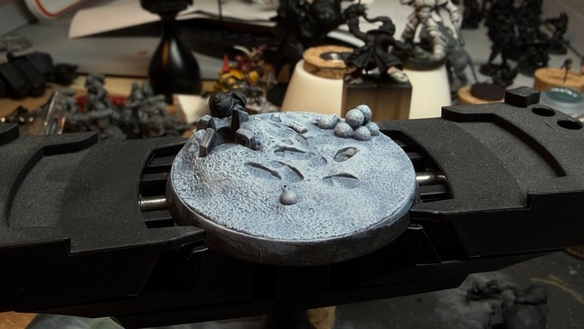 Photo of a large round sculpted base on a painting handle. The base has a sculpted snowy ground with footprints and some snowballs, which has been painted with a slight blue tint to the shadows under the white snow.