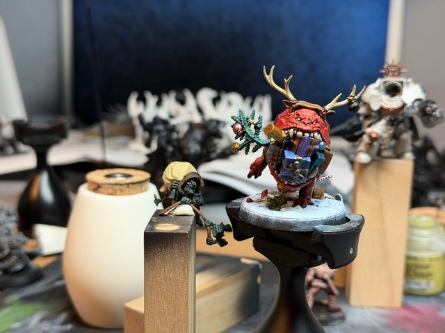 Photograph of the red gobbo stuck to the corner of a narrow wood block, with the squig balanced on its base on a Citadel painting handle.