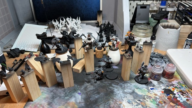 A bunch of rectangular wooden blocks standing upright, with a mix of space marine heads and arms tacked to them for painting. Also a Terminator Captain model fixed to one, in a pale off-white colour scheme.