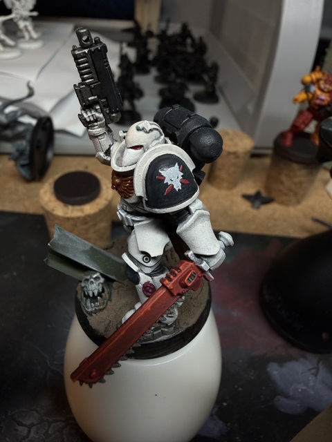 Photo of an in-progress Wolfspear marine holding a chainsword. The pauldron is off-white round the rim with a black inner base and there’s a Wolfspear icon/logo in the centre. Looking closely you can see a slight printing offset on the red spears where a tiny bit of white shows on the left side of each shape