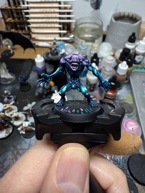 Photograph of an Ur-ghul model, painted with a dark blue base, bright blue-green highlighting for a very high contrast effect. The head and across the shoulders are highlighted with a bright layering of pinks for a similar effect