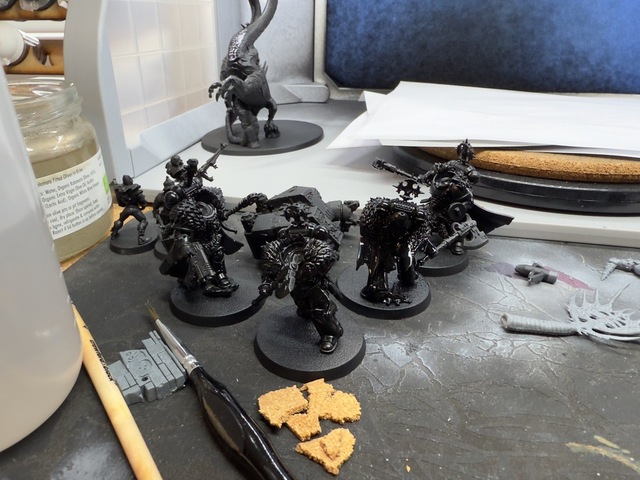 Photograph of a selection of miniatures that have been primed black. They’re all missing heads, which have been kept separate for painting.