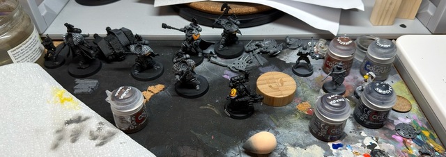 Photograph of a painting area, with various miniatures primed black and beginning to be painted, including some of the new Space Wolf models and an older Deathwatch model with an Imperial Fists shoulder pad painted yellow
