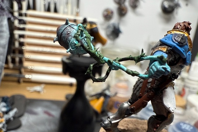 Close-up photograph of a miniature's hand with a pale green-blue-painted paperclip wrapped through the hand and around a rugby/-/NFL-style football. Dabs of green stuff on the paperclip create 'spikes' to mimic lightning crackles.